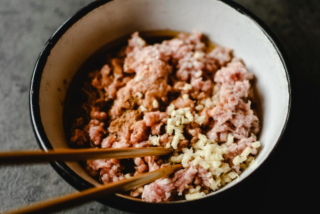 Close-up of uncooked minced pork and chopped garlic in a bowl, emphasized texture.