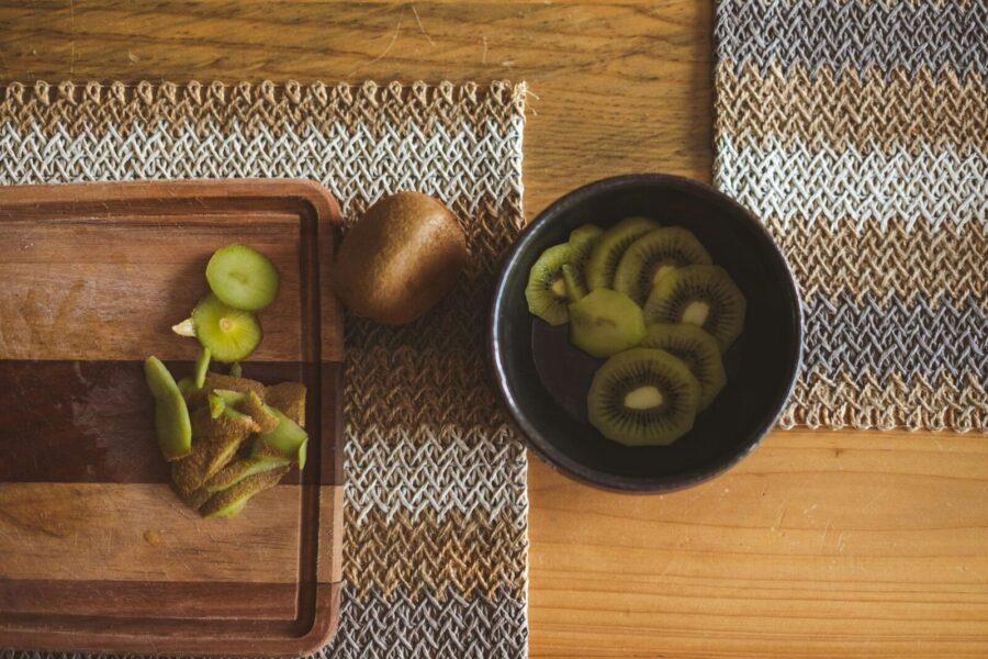 Overhead shot of sliced kiwi on a wooden table with woven placemats, showcasing vibrant fruit and textures.