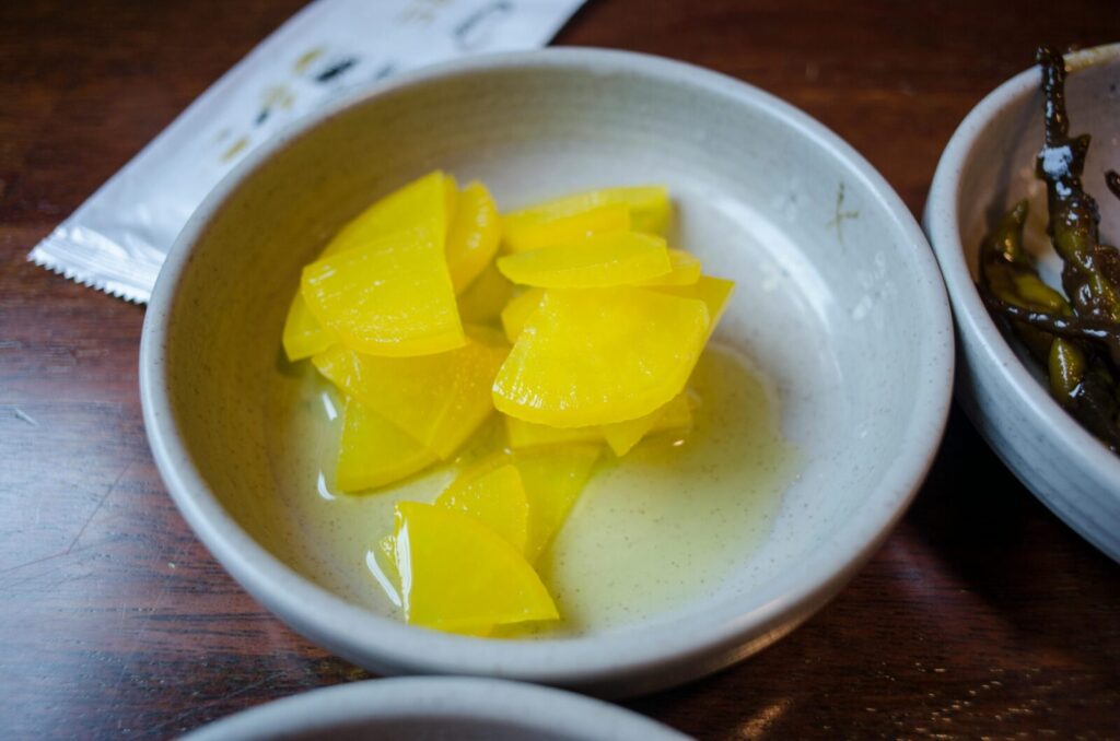 Close-up of sliced yellow pickled daikon radish in a ceramic bowl.