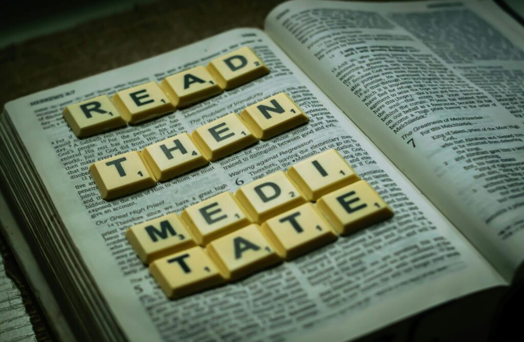 Open Bible with Scrabble tiles spelling 'Read Then Meditate' in a still life composition.