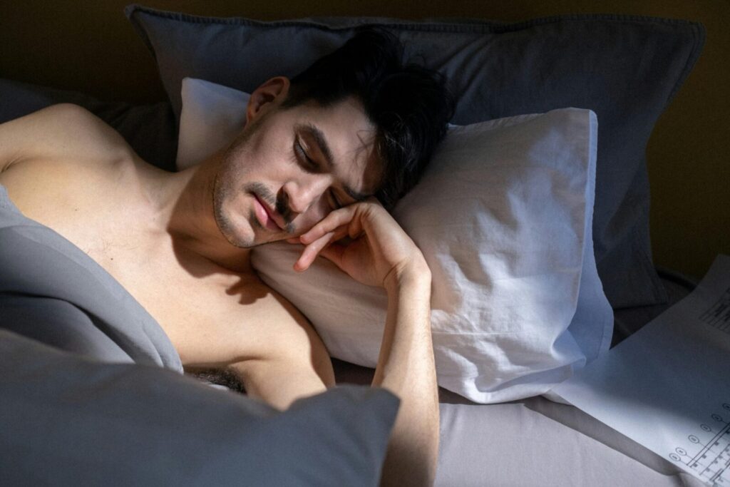 A man peacefully sleeping in a sunlit bedroom with natural light streaming in.