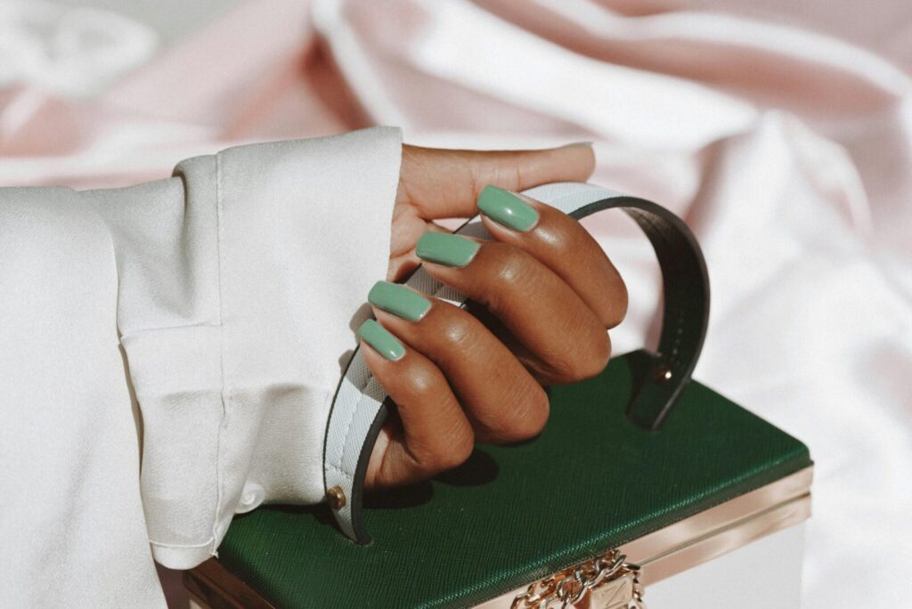 Close-up of a woman's hand with green nails holding a stylish handbag, showcasing fashion and elegance.